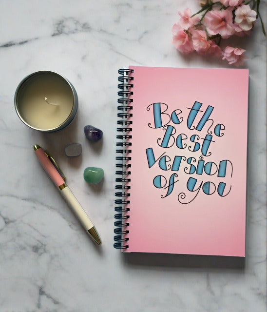 Notebook that reads - be the best version of you. On desk with pen, candle and blossom