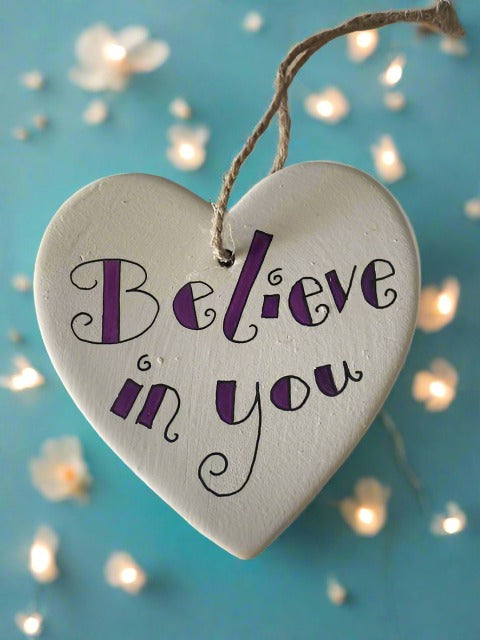white ceramic heart with string, writing on the heart says - believe in you
