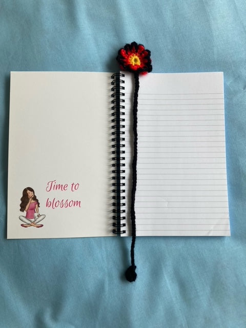 Open notebook with handmade crochet bookmark placed on the top. Inside cover has drawing of girl and words that say time to blossom