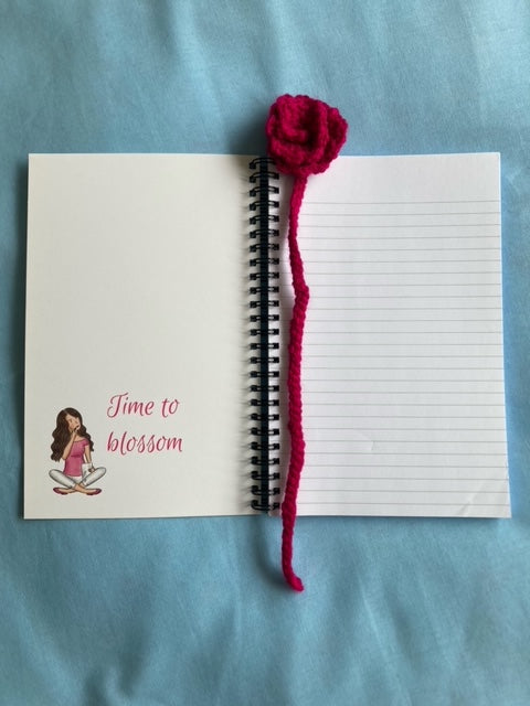 Open notebook with handmade crochet bookmark placed on the top. Inside cover has drawing of girl and words that say time to blossom
