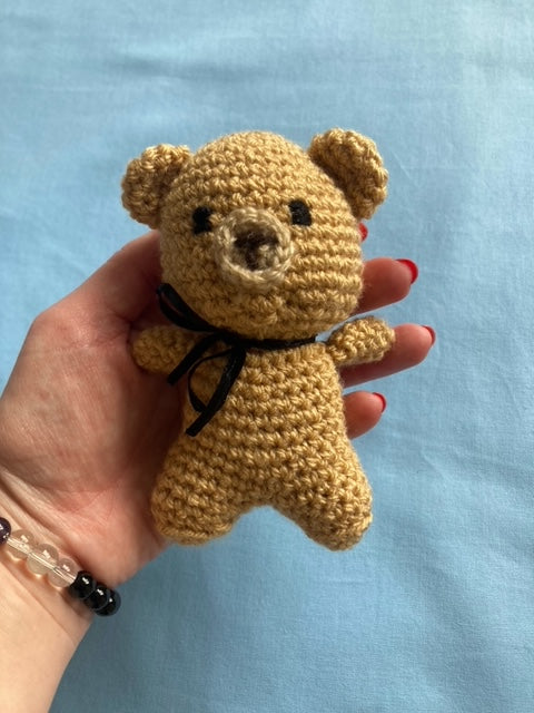 Hand holding crochet bear that is brown with a black neck tie