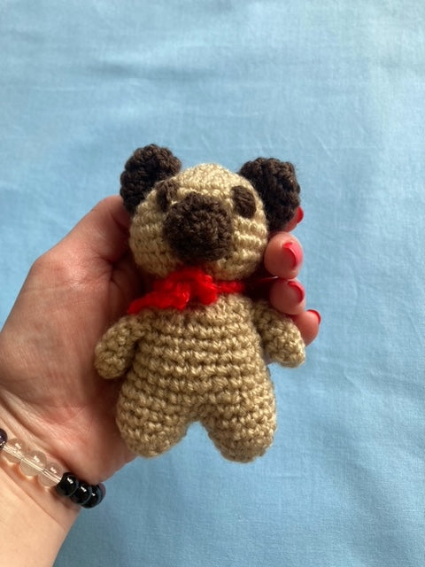 Hand holding crochet bear that is brown with a red neck tie