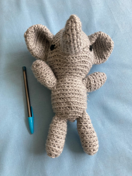 handmade crochet elephant, grey. With pen next to it on ablue background