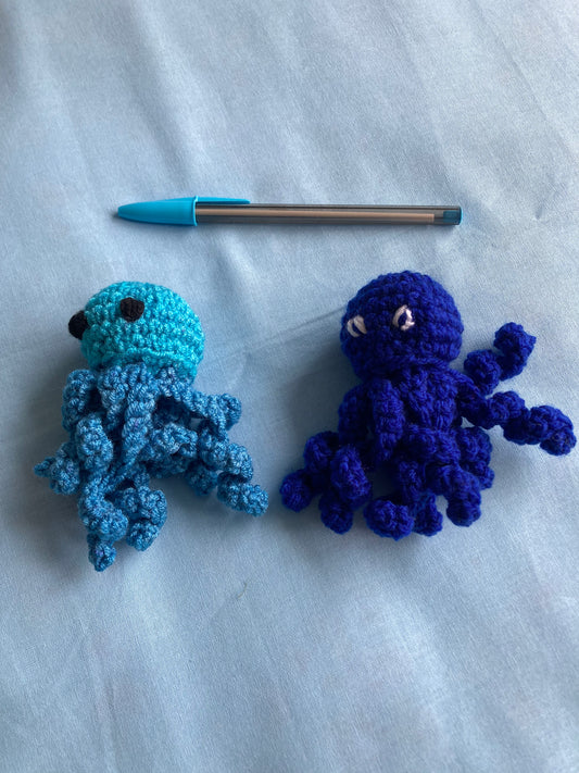 2 handmade crochet octopus, blue with pen above on a blue background