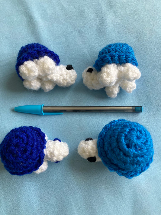 4 Handmade crochet turtles, white head and legs with blue shell. With pen next to them on a blue background