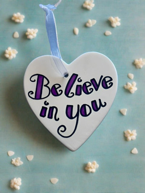 White ceramic heart with white ribbon, writing on heart reads - believe in you
